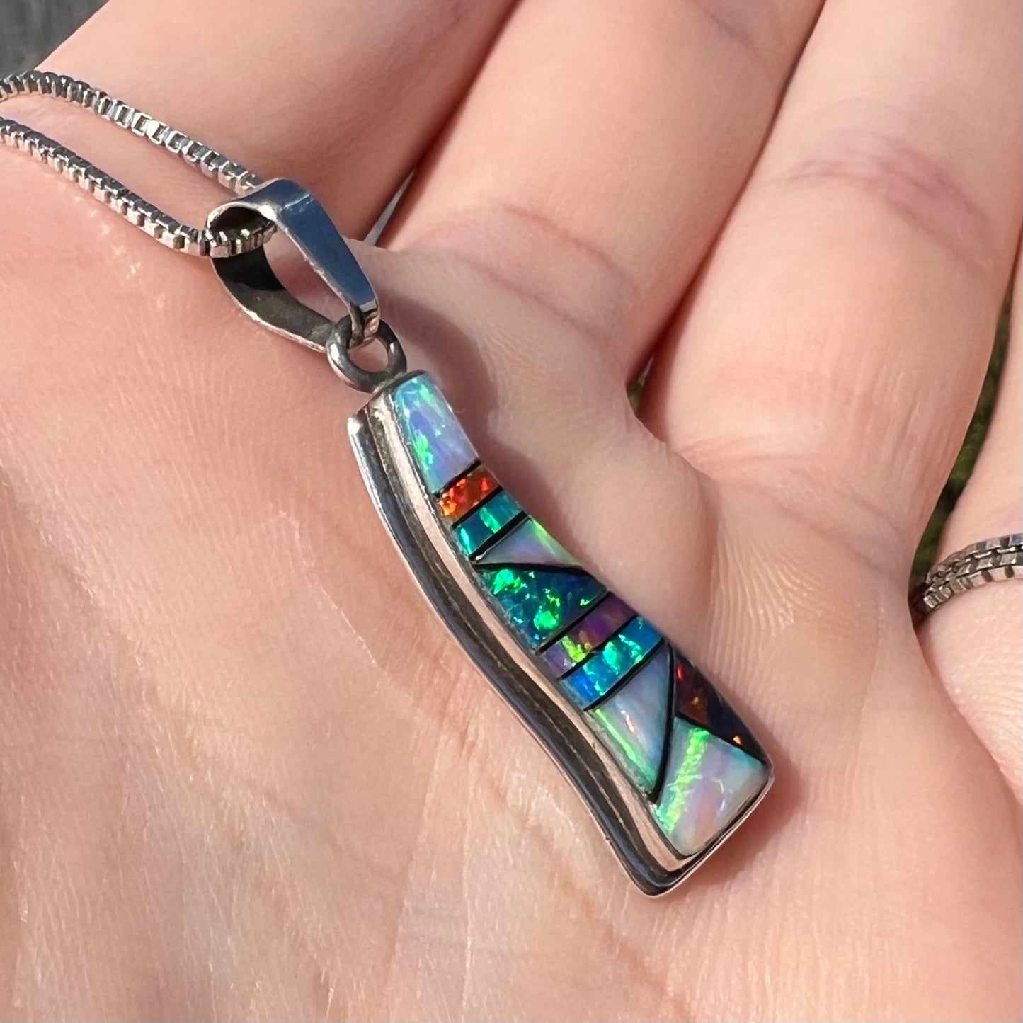 A synthetic opal inlay necklace, held in a hand and shown at an angle in sunlight.