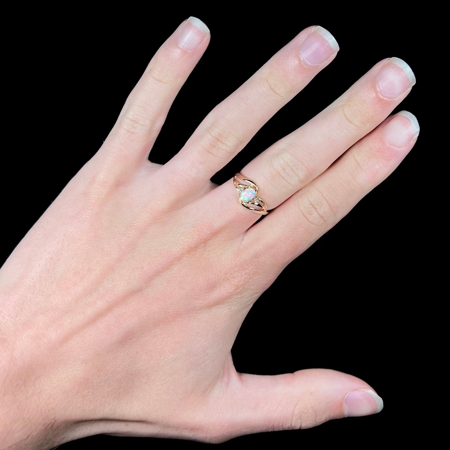A yellow gold ring mounted with two diamond accents and an oval cut lab created opal. The opal has bright red colors.