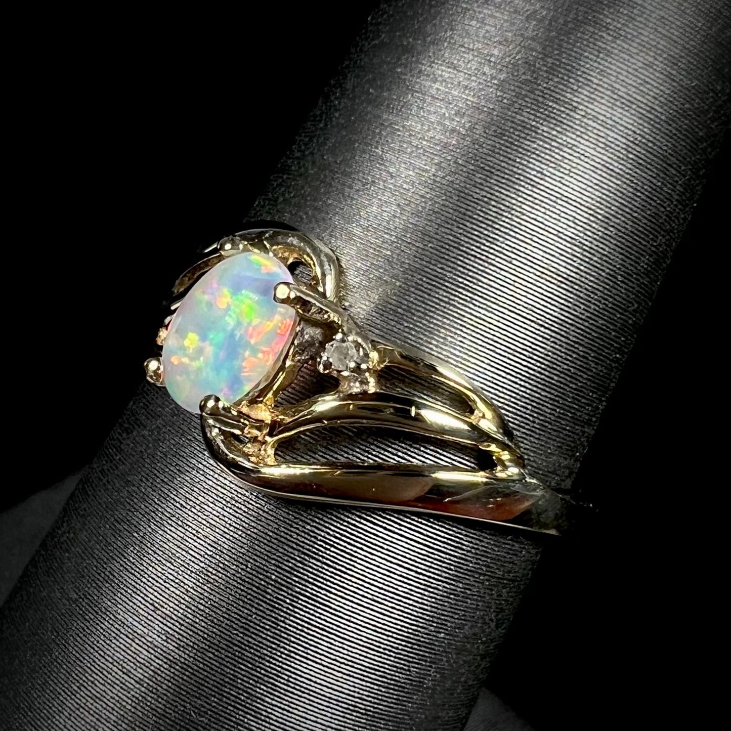 A yellow gold ring mounted with two diamond accents and an oval cut lab created opal. The opal has bright red colors.