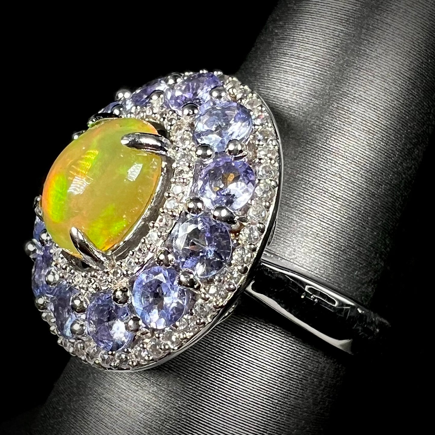 Angled view of tanzanite halo ring set with Ethiopian fire opal in center against black background.