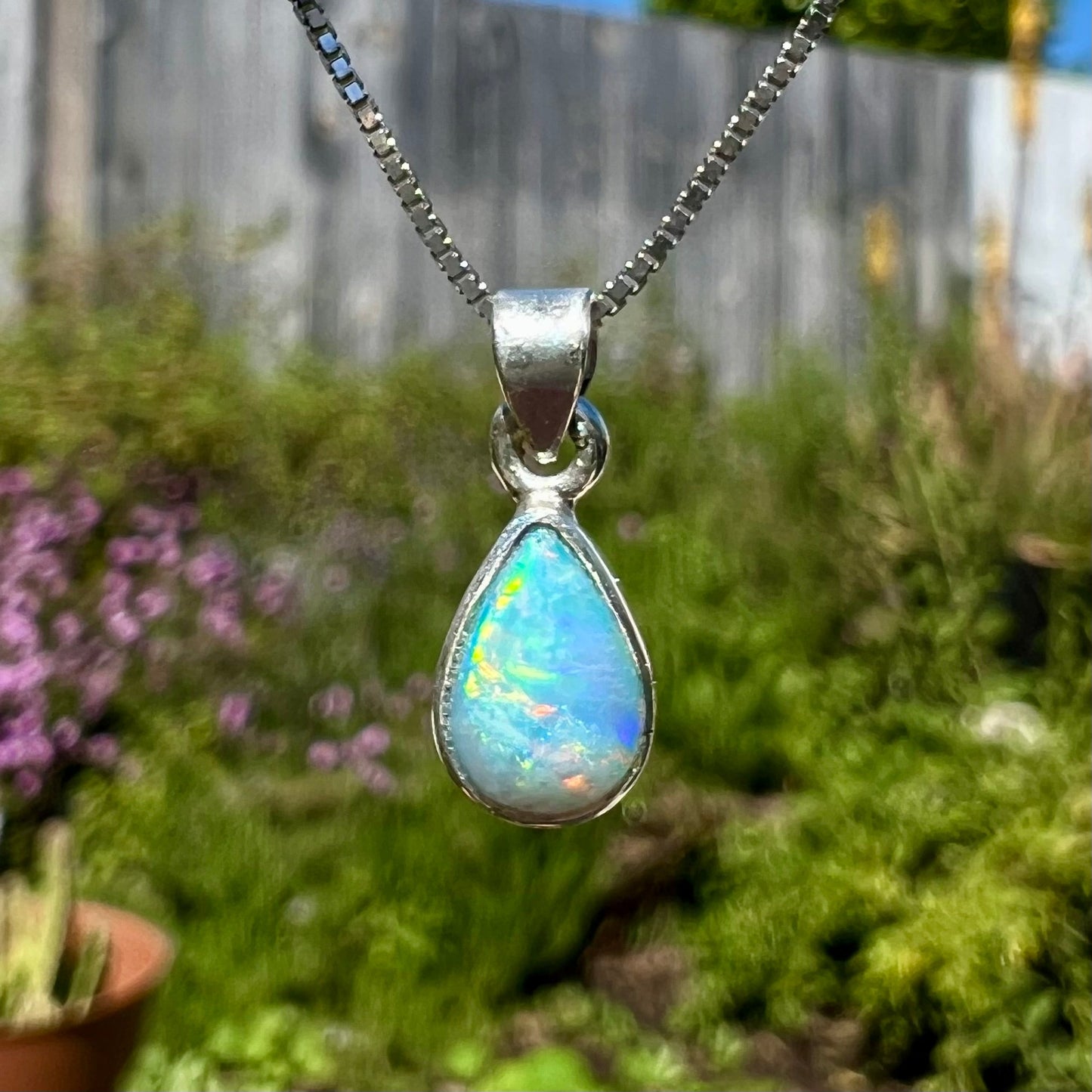 A dainty, sterling silver necklace bezel set with a natural, pear shaped opal stone.