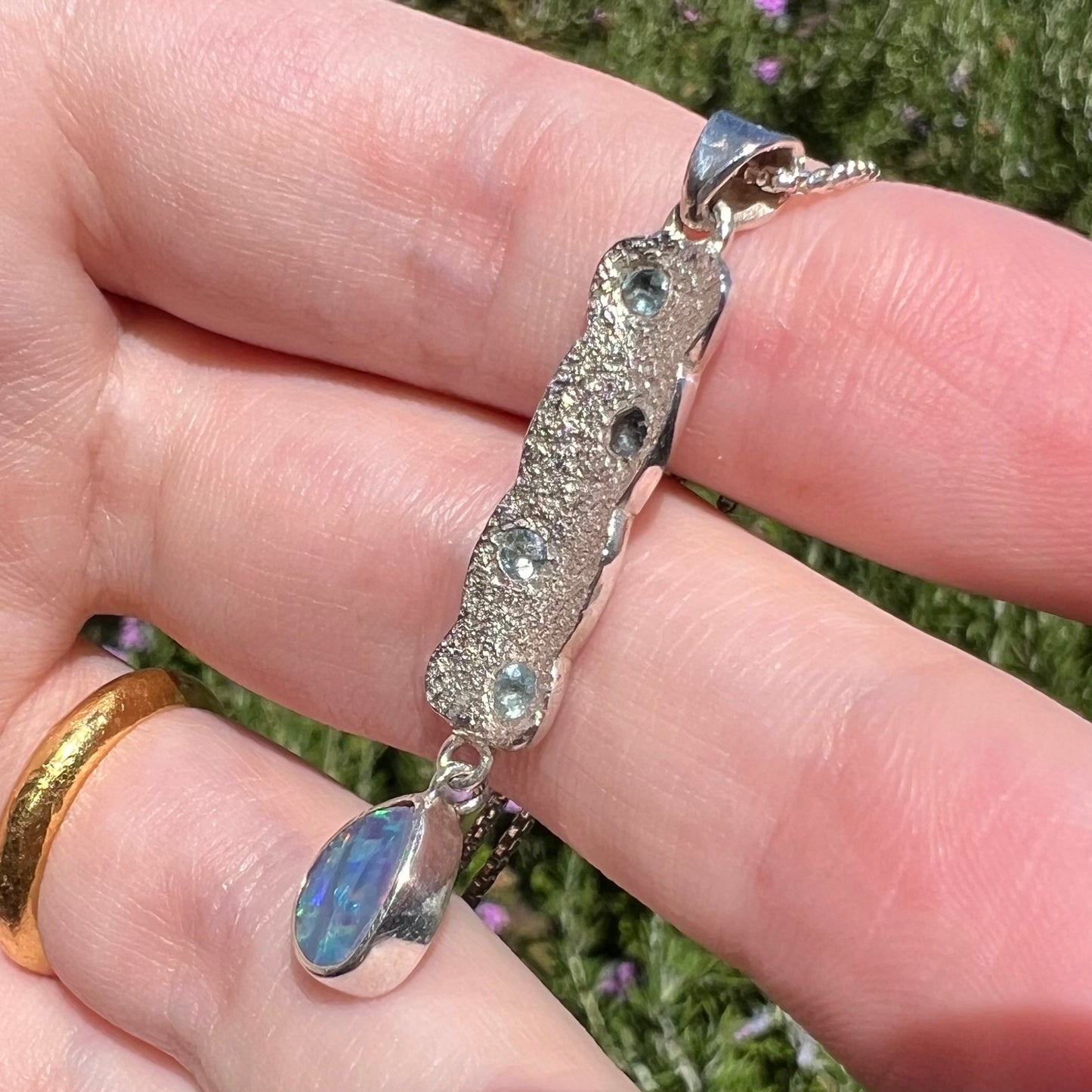 Close-up side view of a sterling silver opal drop pendant with a textured design, shown in natural sunlight.