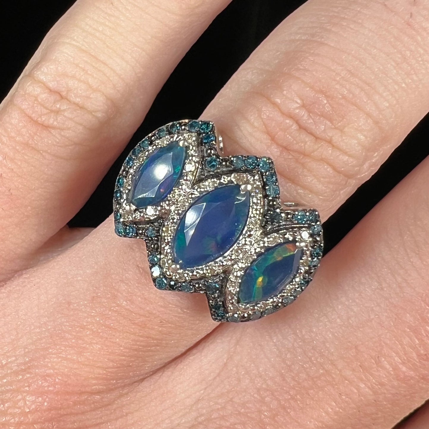Front view of a three-stone blue opal ring with blue and white diamond accents, worn on a finger.
