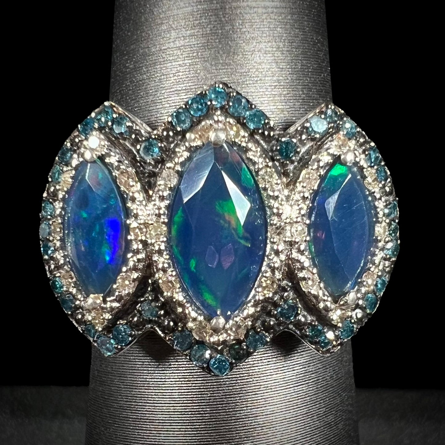 A three-stone marquise opal and blue diamond ring in silver, shown straight-on against a black background.