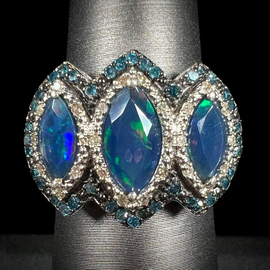 A three-stone marquise opal and blue diamond ring in silver, shown straight-on against a black background.