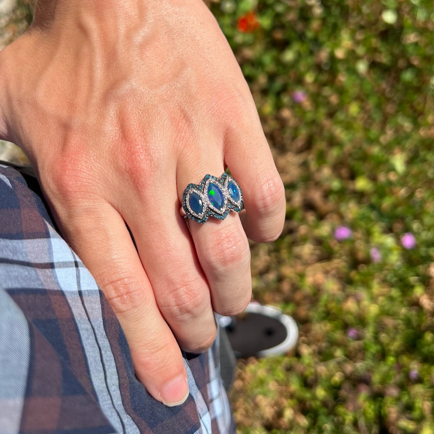 A three-stone opal ring worn on a person's hand as they rest it on their hip in natural light.