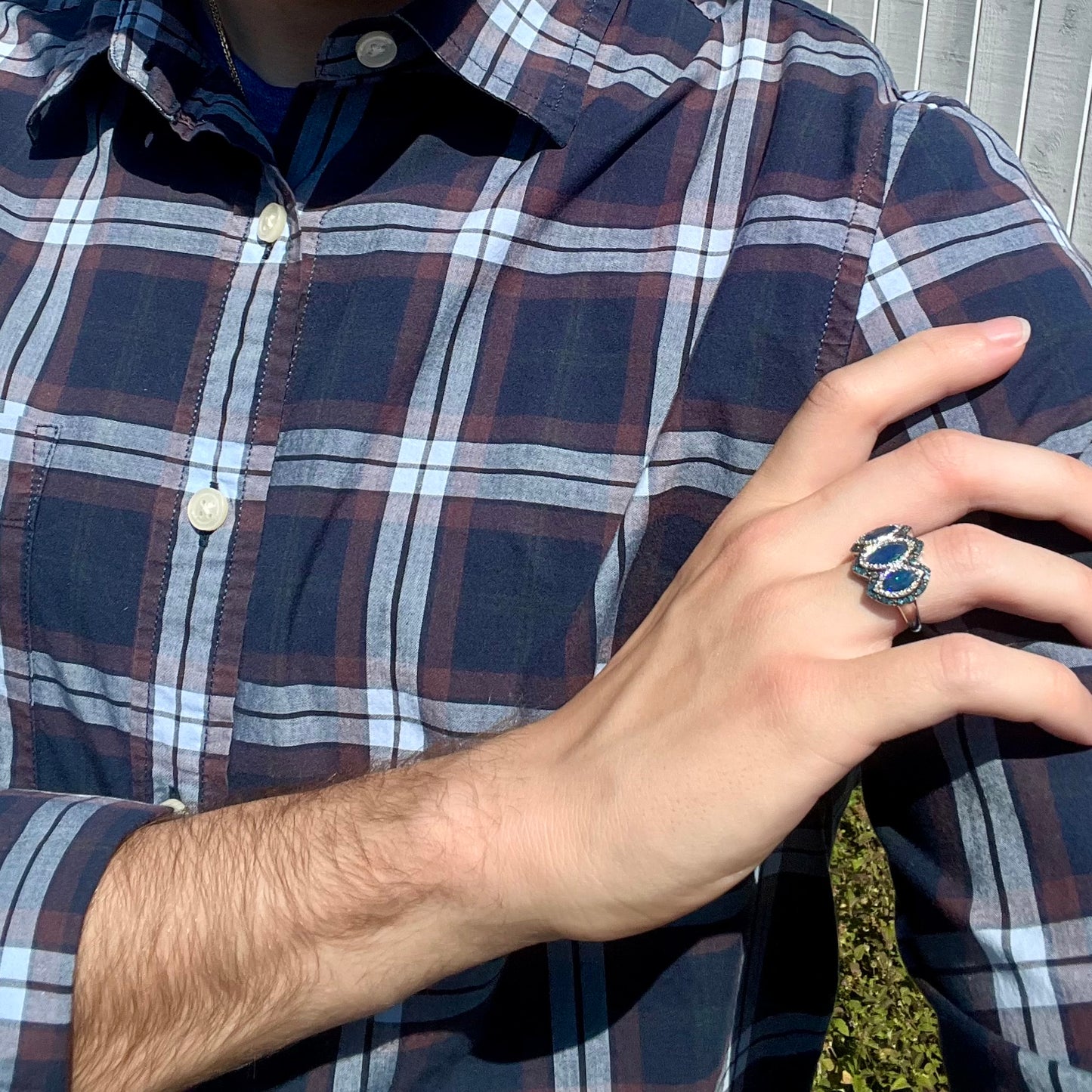 A person crossing their arm to hold their shoulder, wearing a three-stone opal and diamond halo ring on their hand.