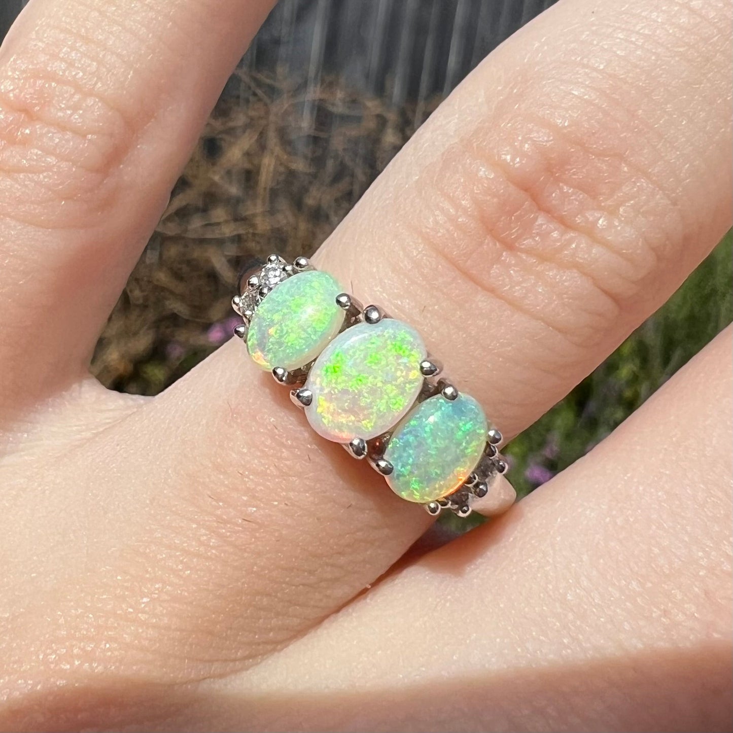 A ladies' white gold ring prong-set with three natural white opals and diamond accents. The opals play a green color.