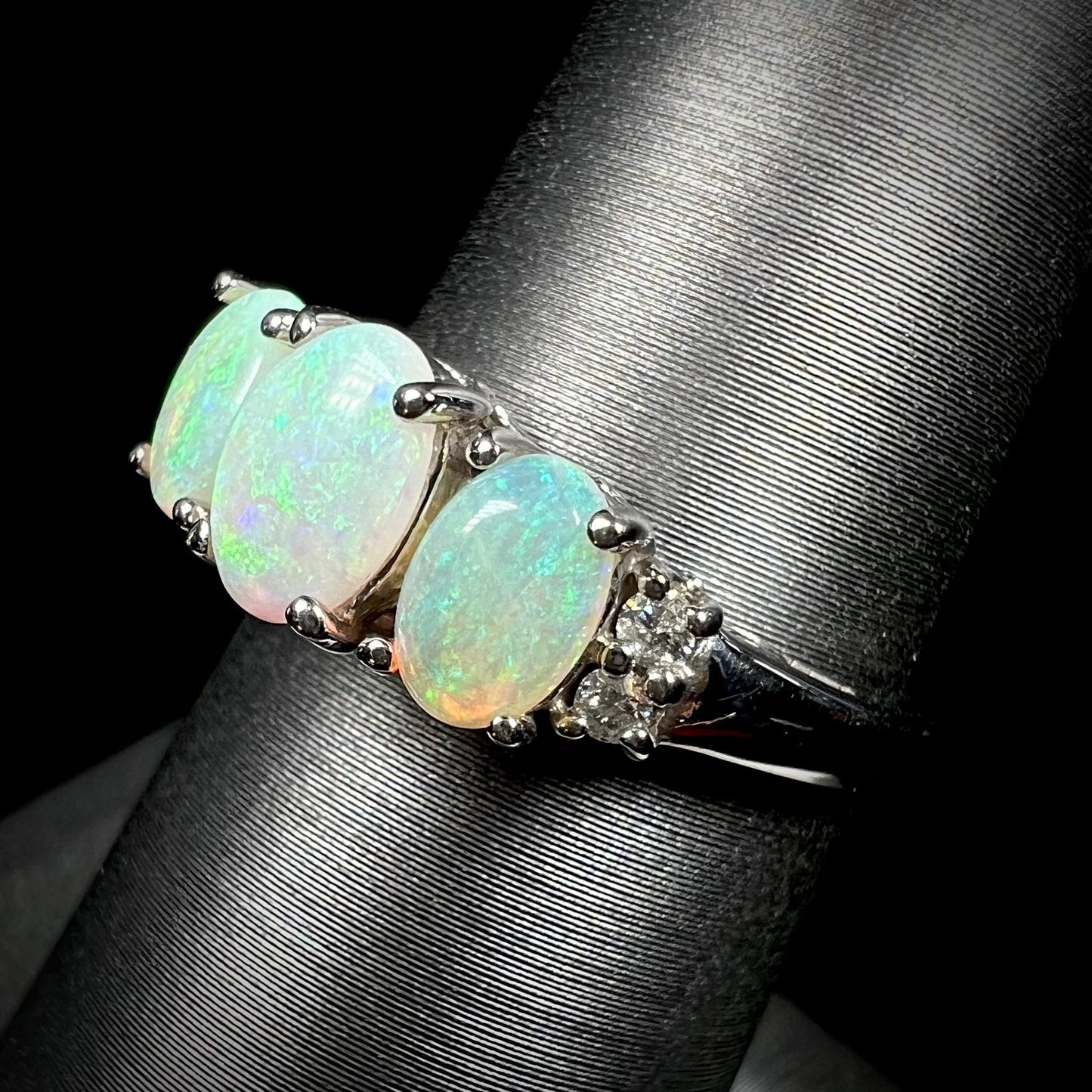A ladies' white gold ring prong-set with three natural white opals and diamond accents. The opals play a green color.