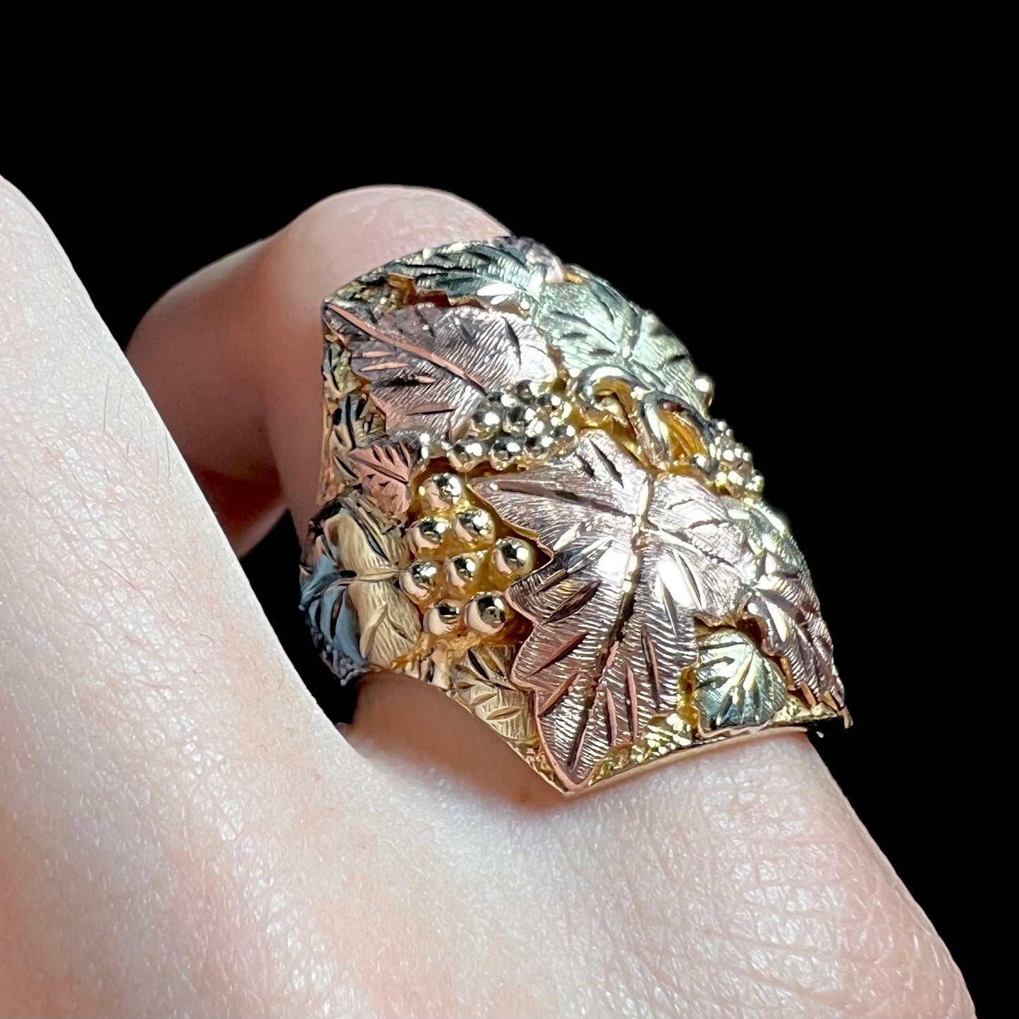 A men's solid gold ring. The ring is Black Hills gold featuring a grapevine and leaf motif with rose and green gold designs.