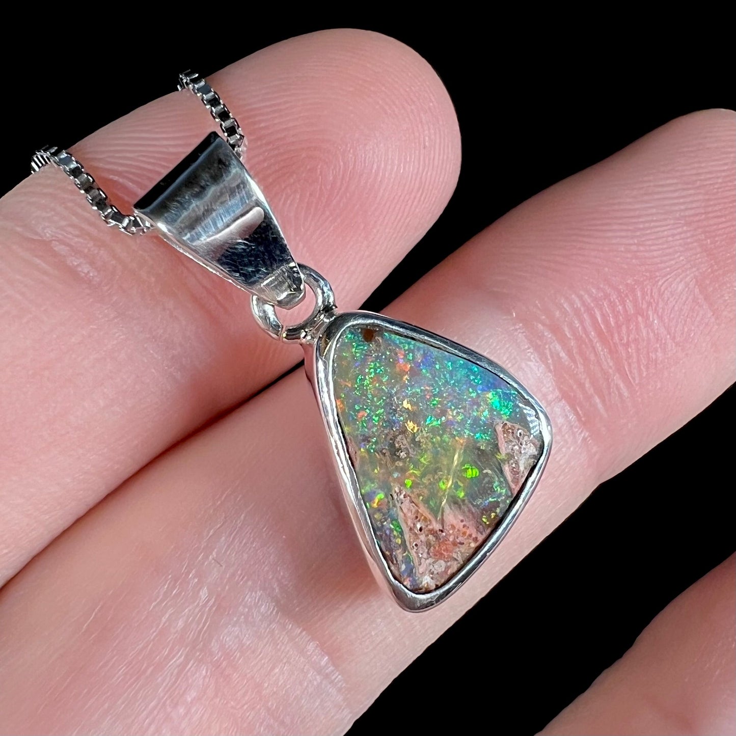 A sterling silver boulder opal necklace on a box chain. The opal twinkles bright red, green, and blue colors.
