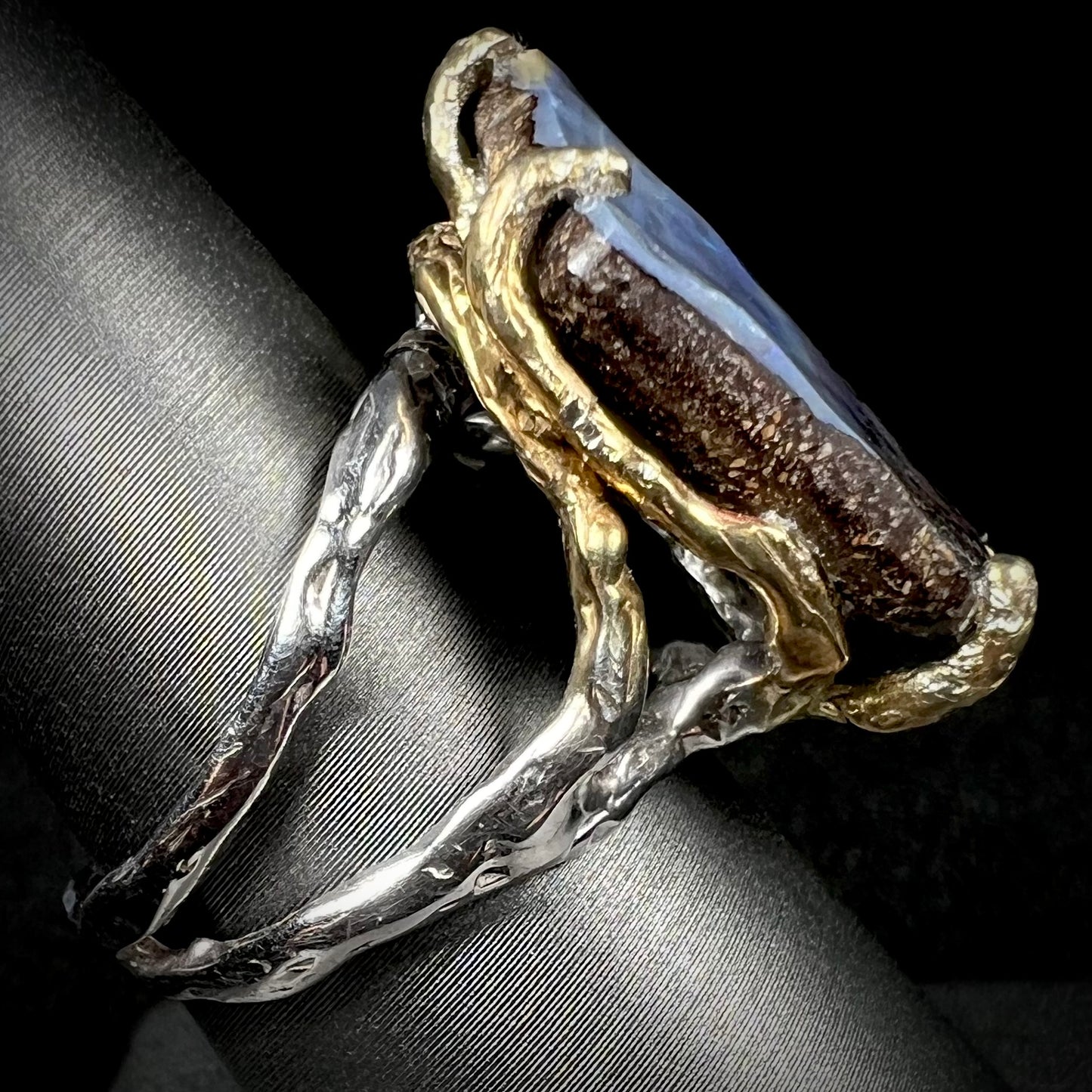 Side view of a two-tone boulder opal solitaire ring. The shank is silver and the prongs are gold plated silver.