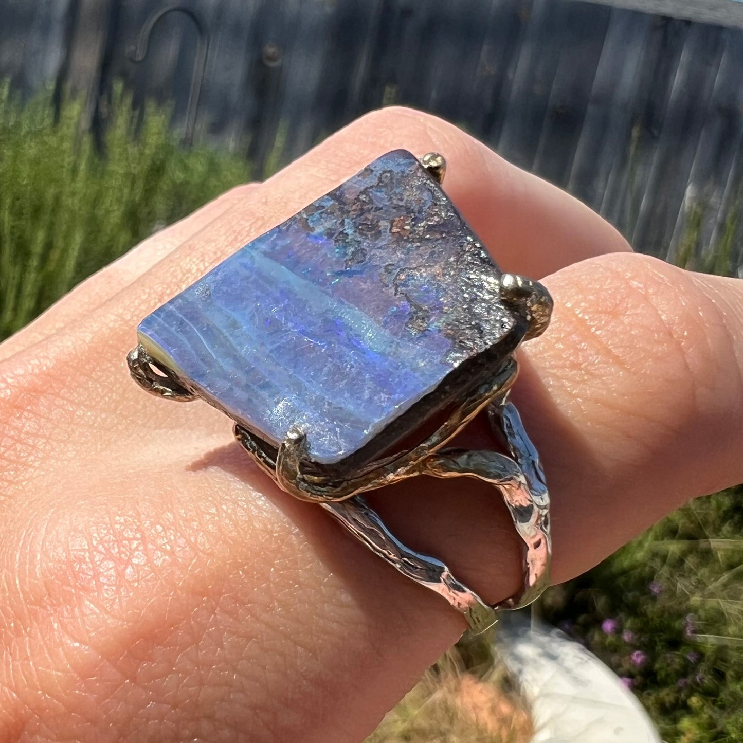 A unisex boulder opal ring worn on a finger, shown at an angle, in the sun. The opal does not show any color play.