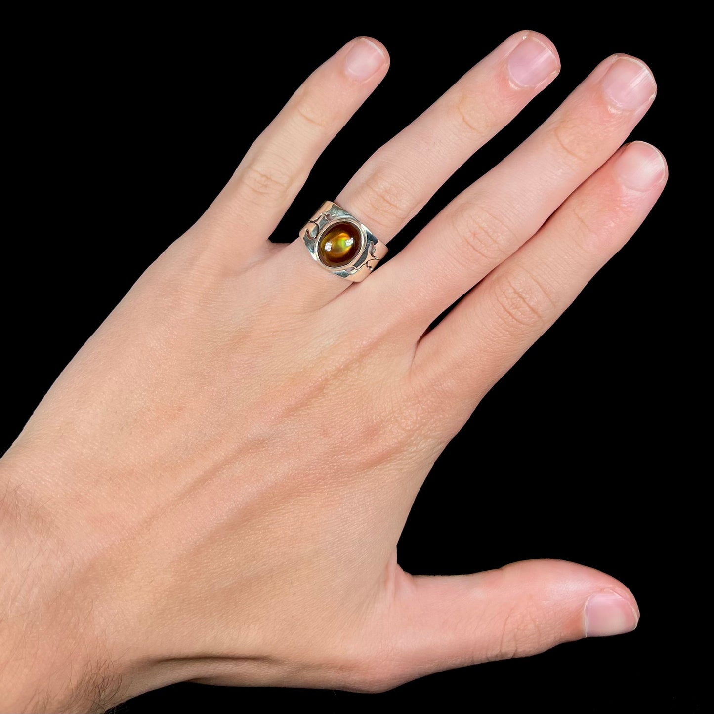 A unisex Mexican fire agate ring made from sterling silver worn on a hand against a black background.