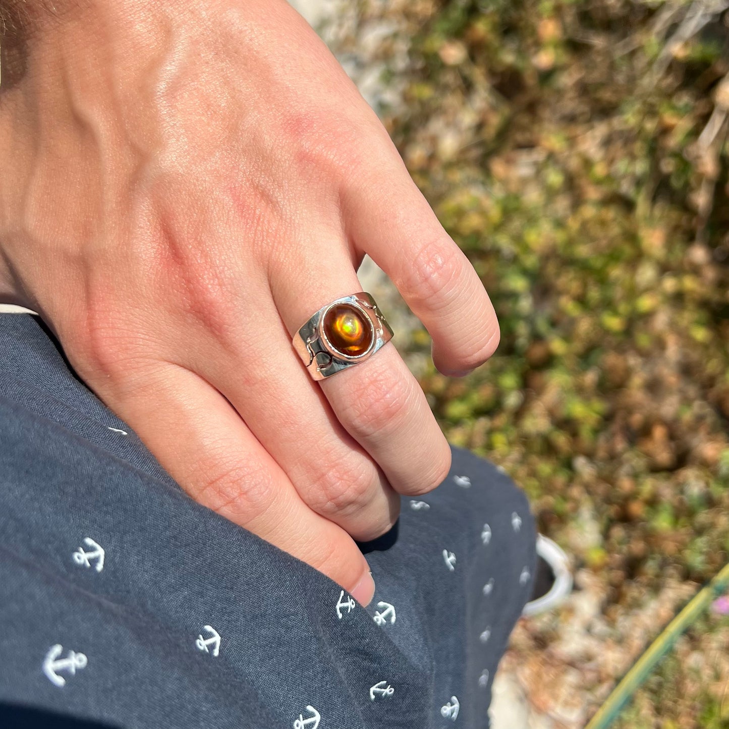 A hand resting on a hip in the sunlight while wearing a silver unisex fire agate ring with a wide band.