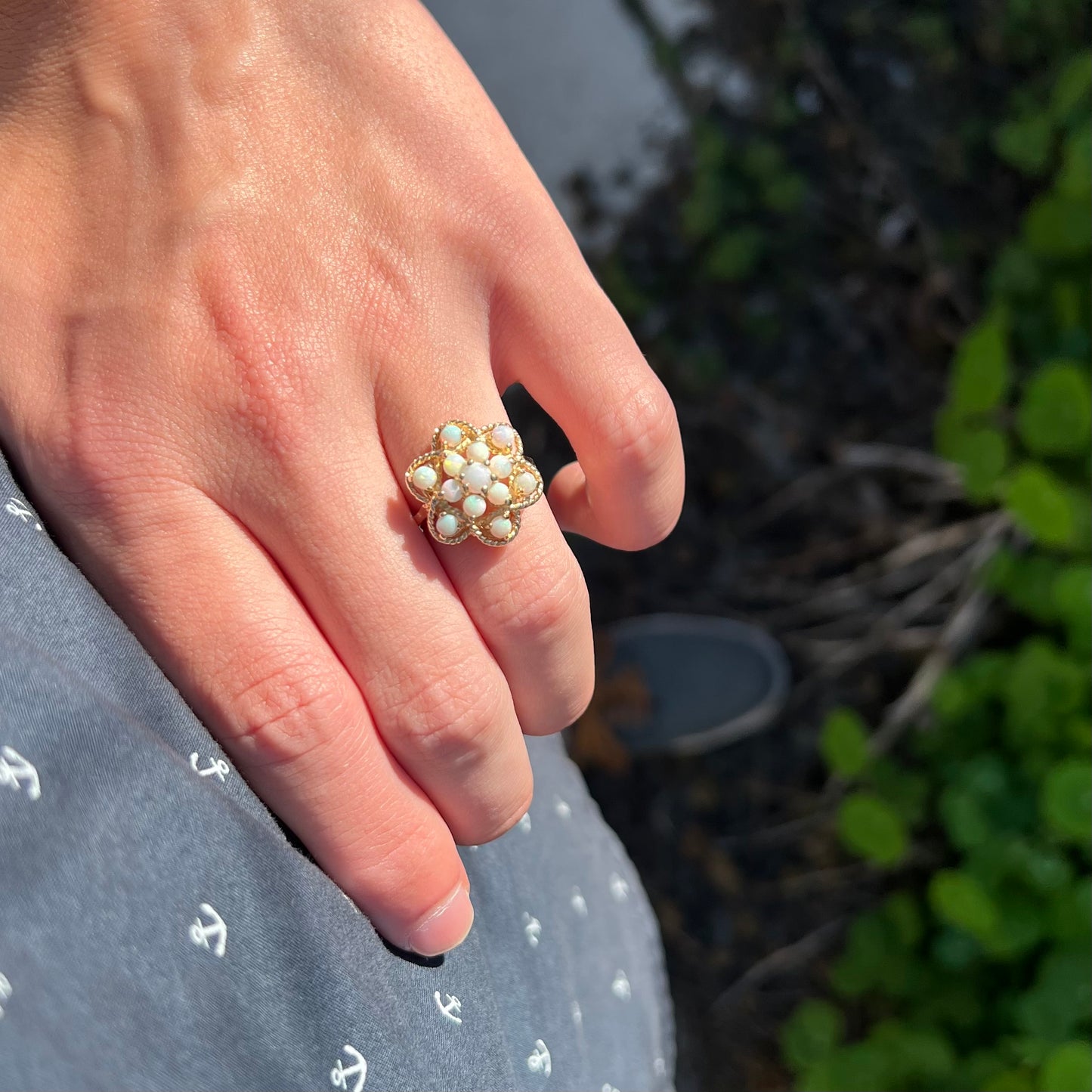 A vintage Australian opal cluster ring with a yellow gold atomic motif, worn on a hand in the sunlight as the hand rests on the model's hip.