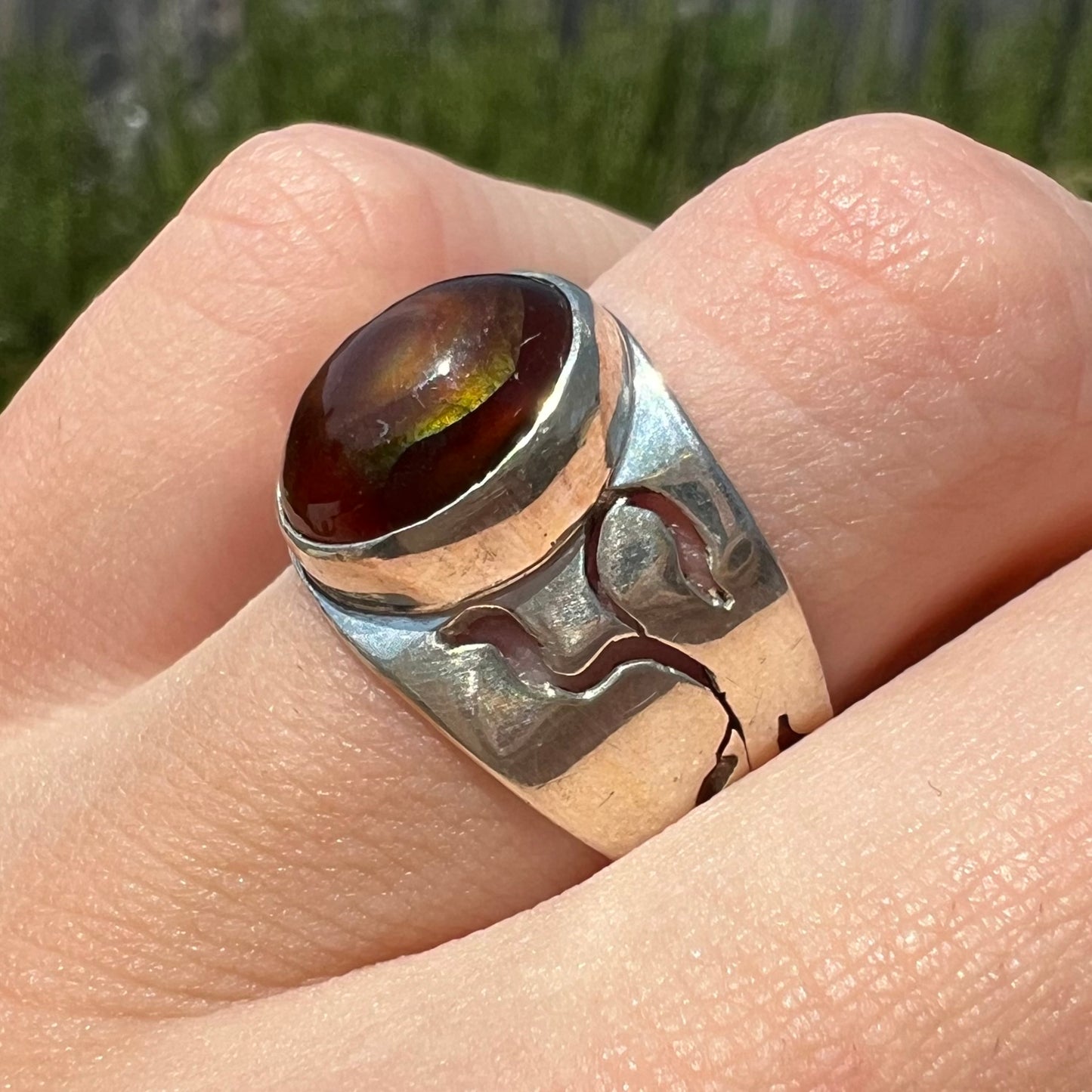 A vintage silver fire agate ring worn on a finger and shown close-up in the sun at an angle.
