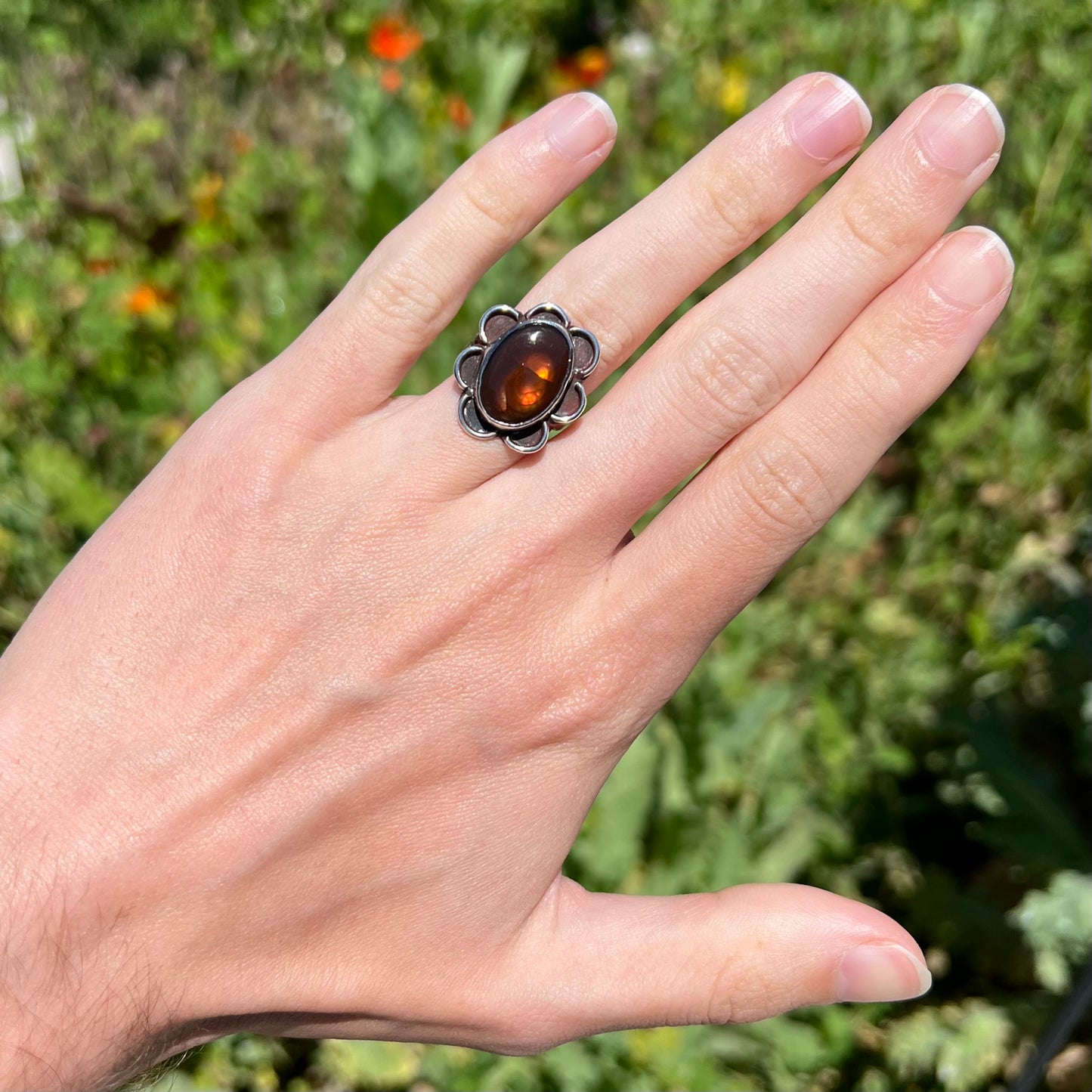 Fire agate ring worn outdoors with orange color play and greenery.