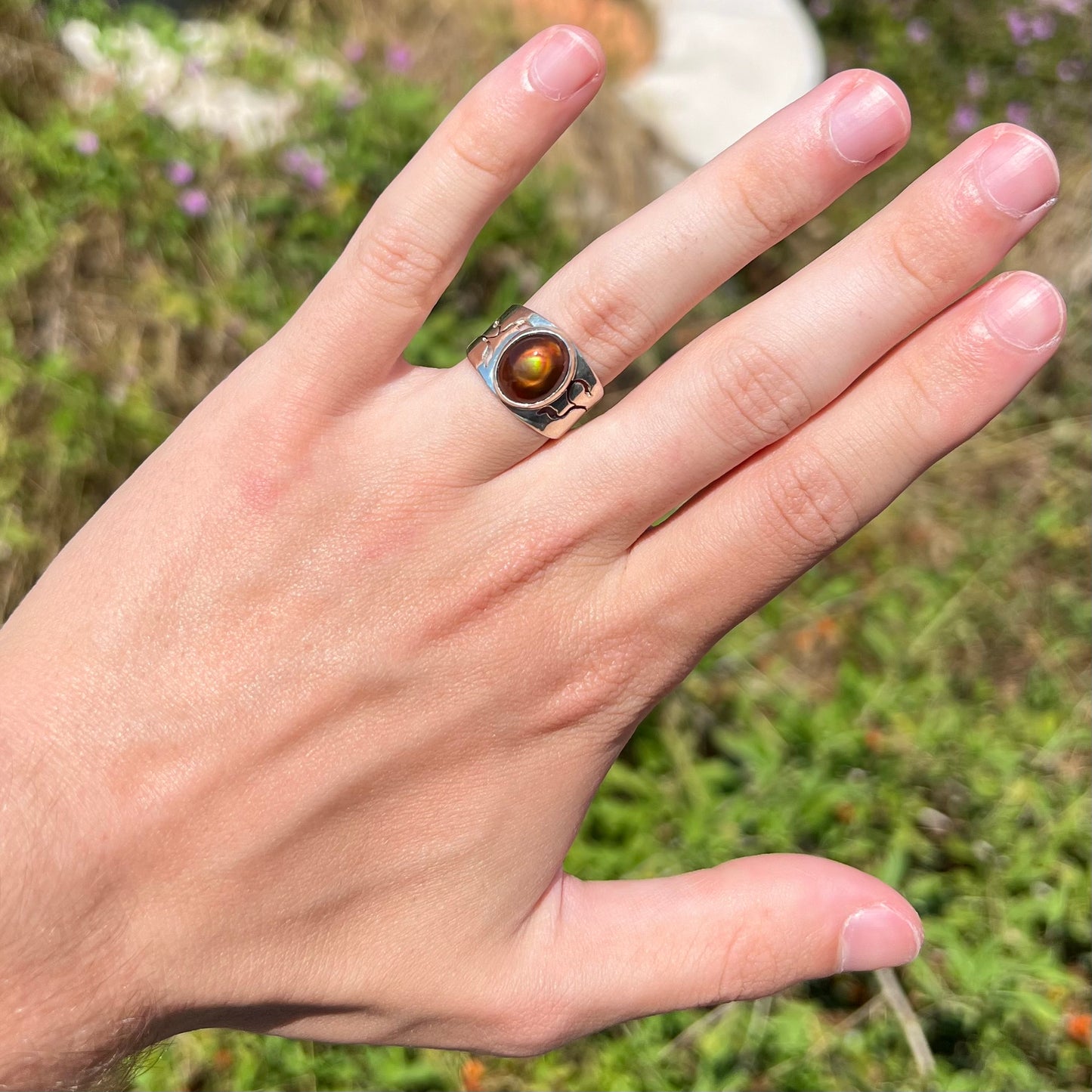 A vintage, silver unisex fire agate ring, worn on a hand in the sunlight against an outdoor backdrop.