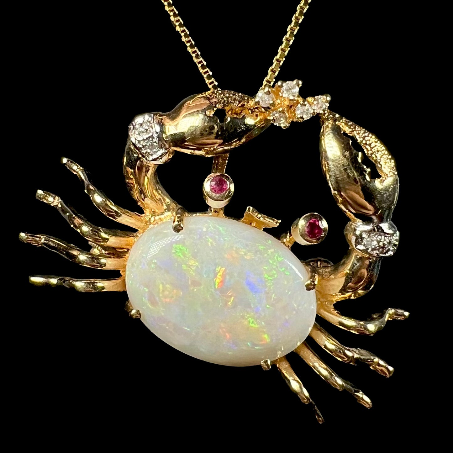 A vintage 14k gold crab pendant and brooch against a black background, featuring a Coober Pedy opal with green and red flashes.