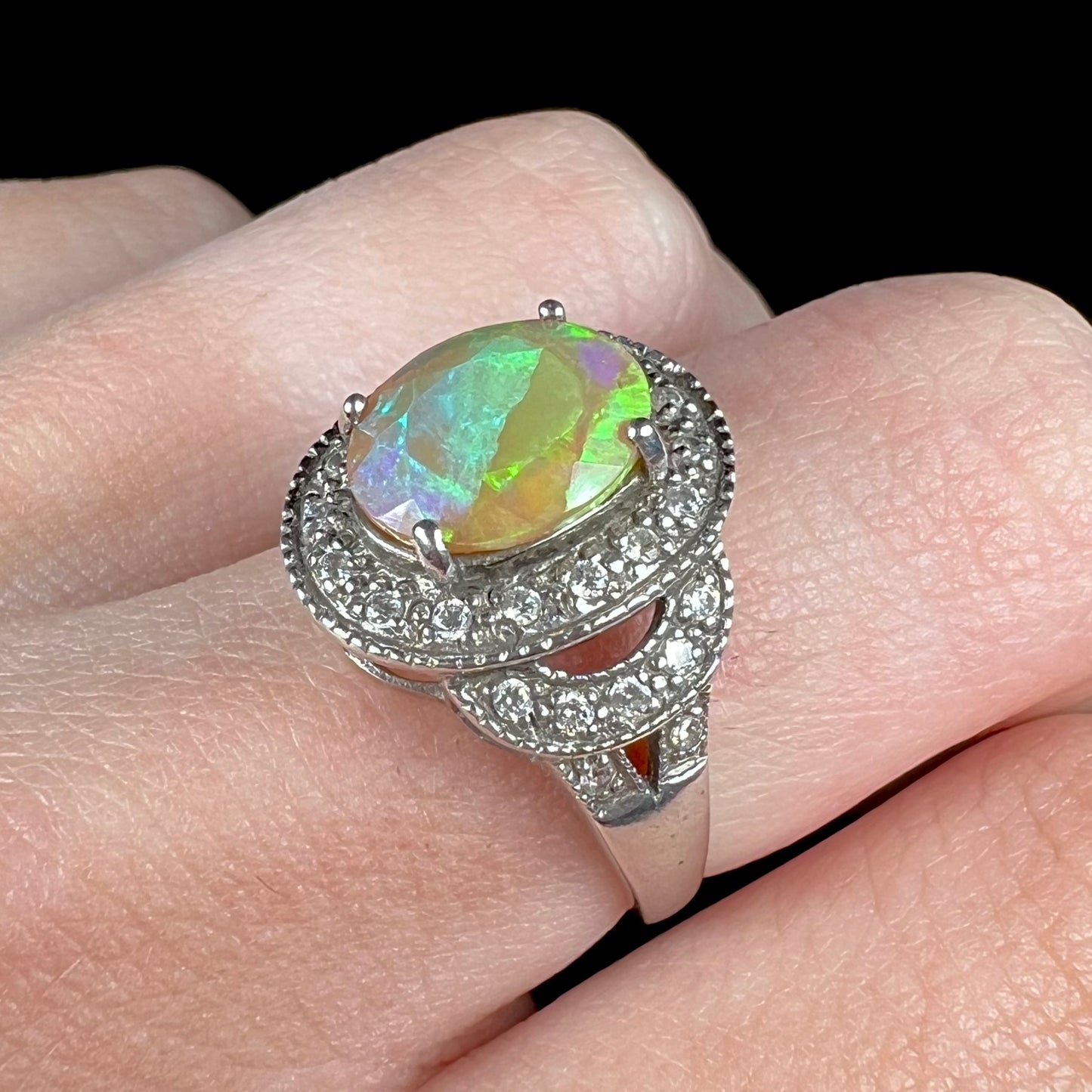A vintage-inspired Ethiopian opal ring with a CZ halo worn on a finger, shown at an angle.