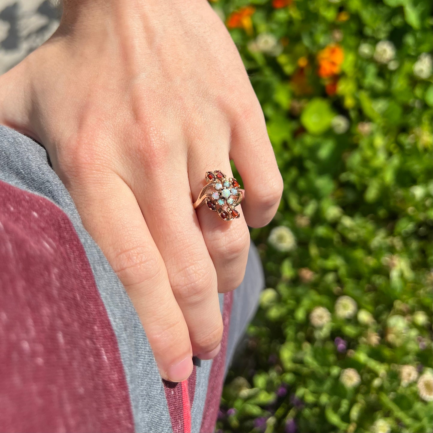 Ring on hand resting on hip, sunlight highlighting opals with greenery in background.
