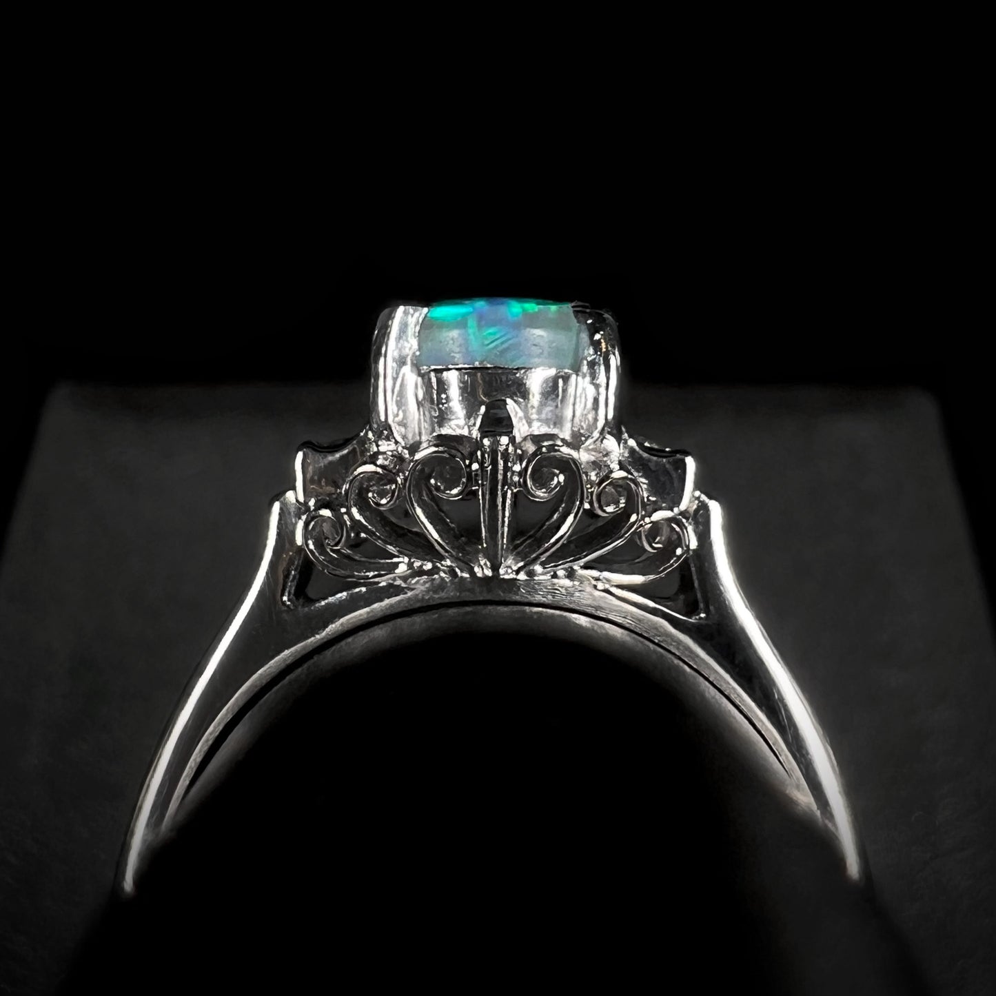 The underside of a vintage platinum black opal engagement ring, showcasing intricate filigree metalwork and diamond-accented gallery details.