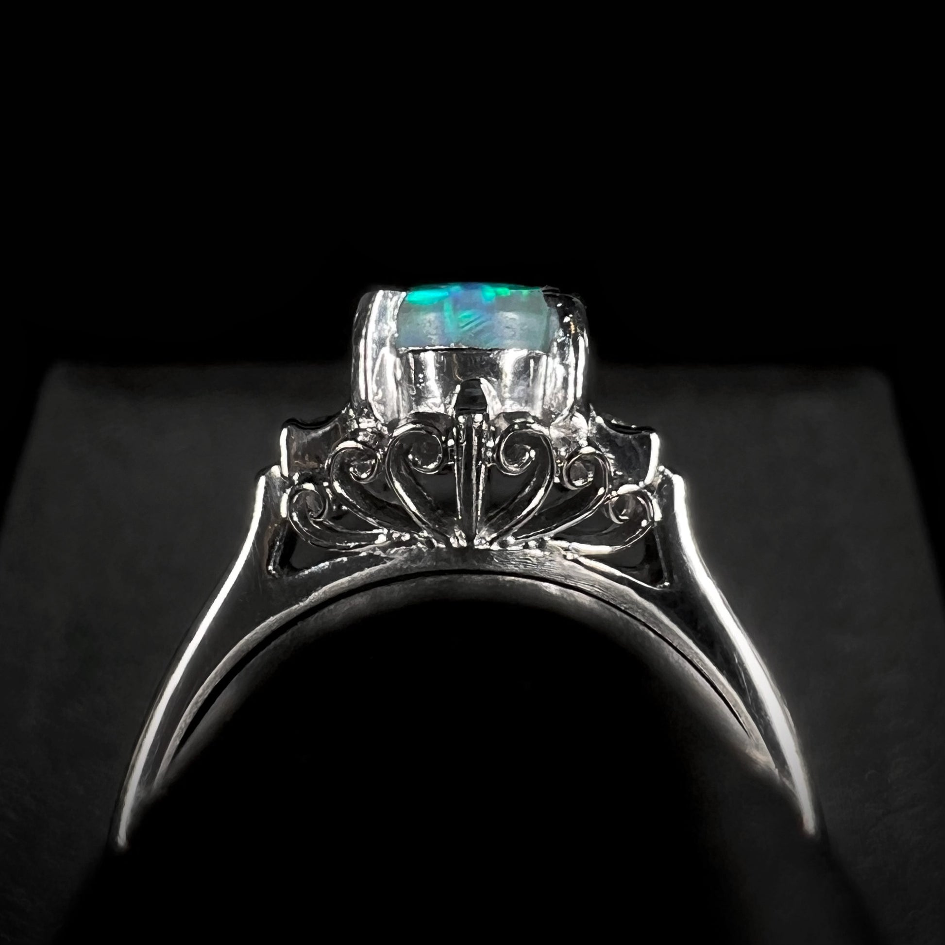 The underside of a vintage platinum black opal engagement ring, showcasing intricate filigree metalwork and diamond-accented gallery details.