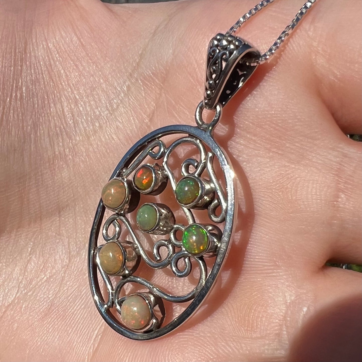 A sterling silver Ethiopian opal filigree necklace shown close-up in a hand in sunlight.