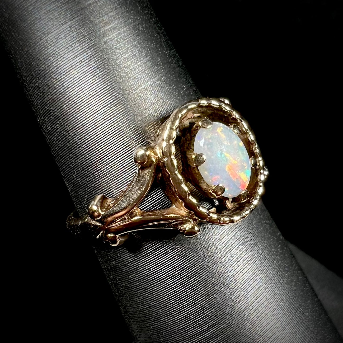 A ladies' Art Nouveau style opal solitaire ring. The mounting is yellow gold with filigree accents.