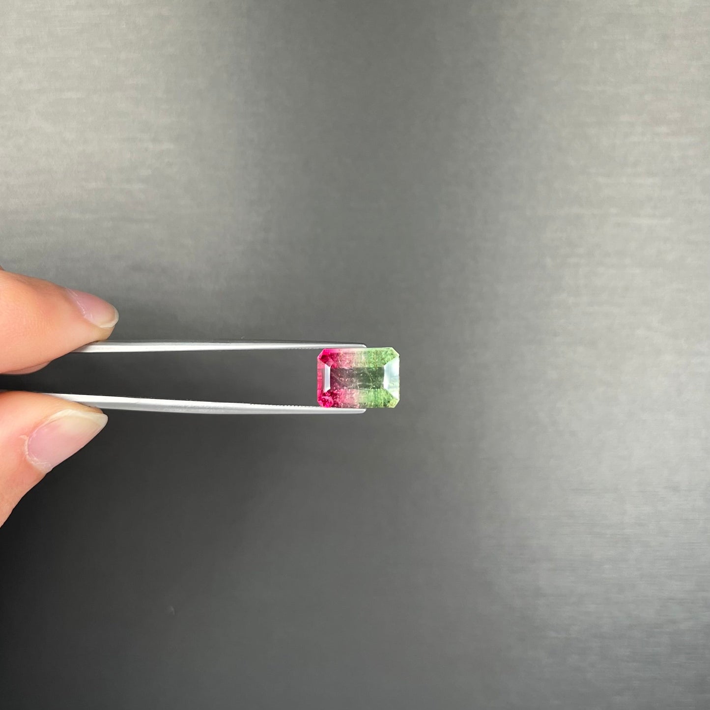 A loose watermelon tourmaline gemstone. The stone is emerald cut and fades from hot pink to green.