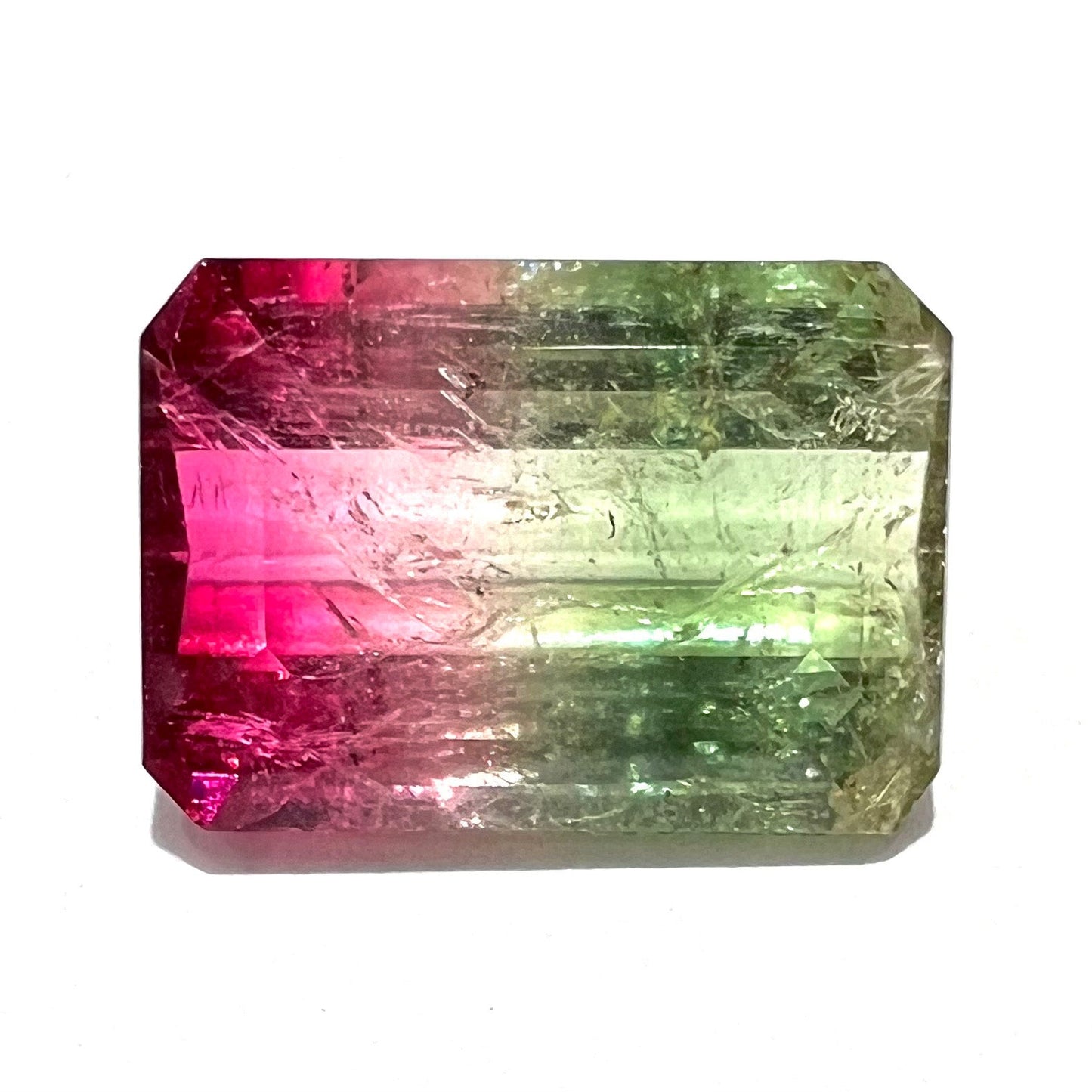 A loose watermelon tourmaline gemstone. The stone is emerald cut and fades from hot pink to green.