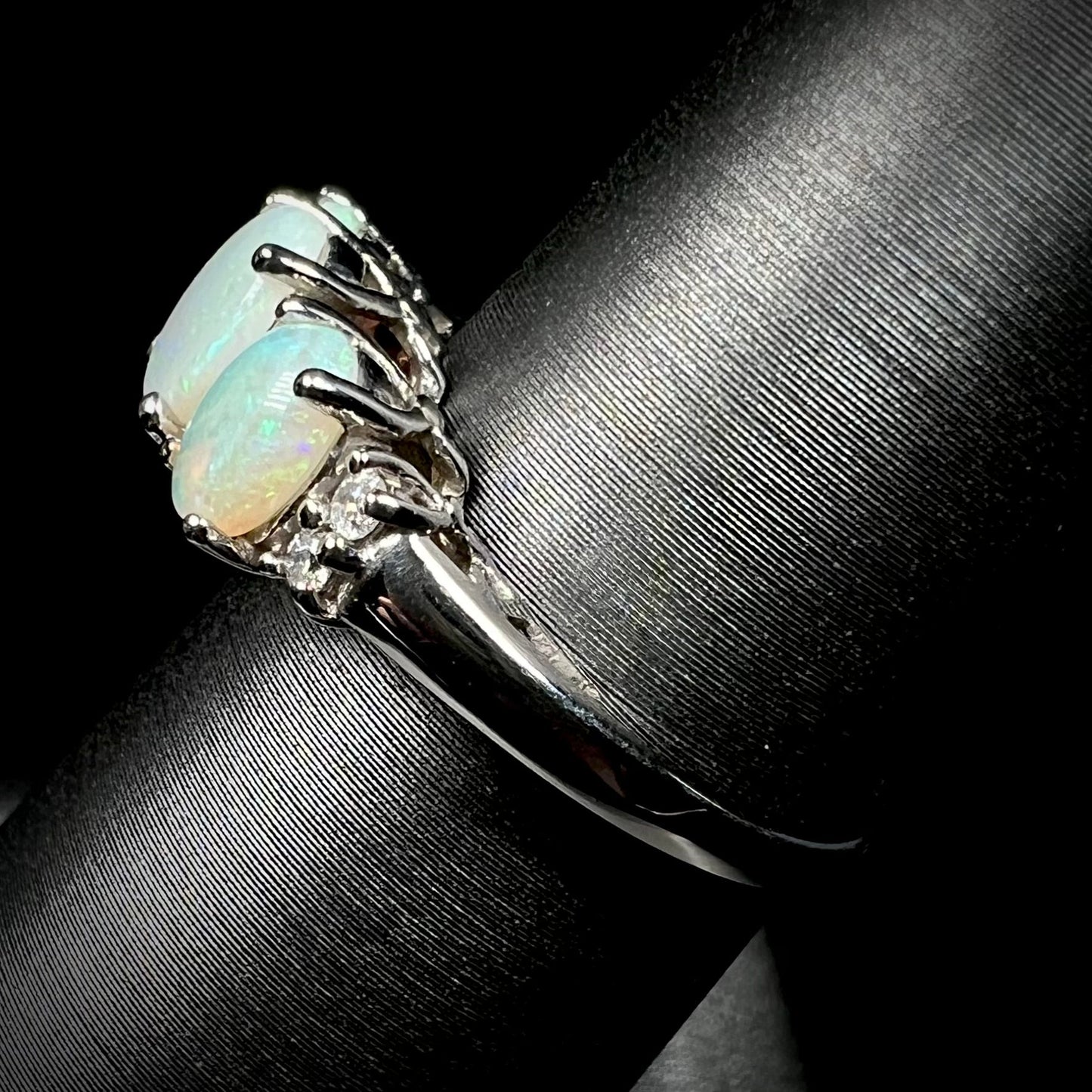 A ladies' white gold ring prong-set with three natural white opals and diamond accents. The opals play a green color.