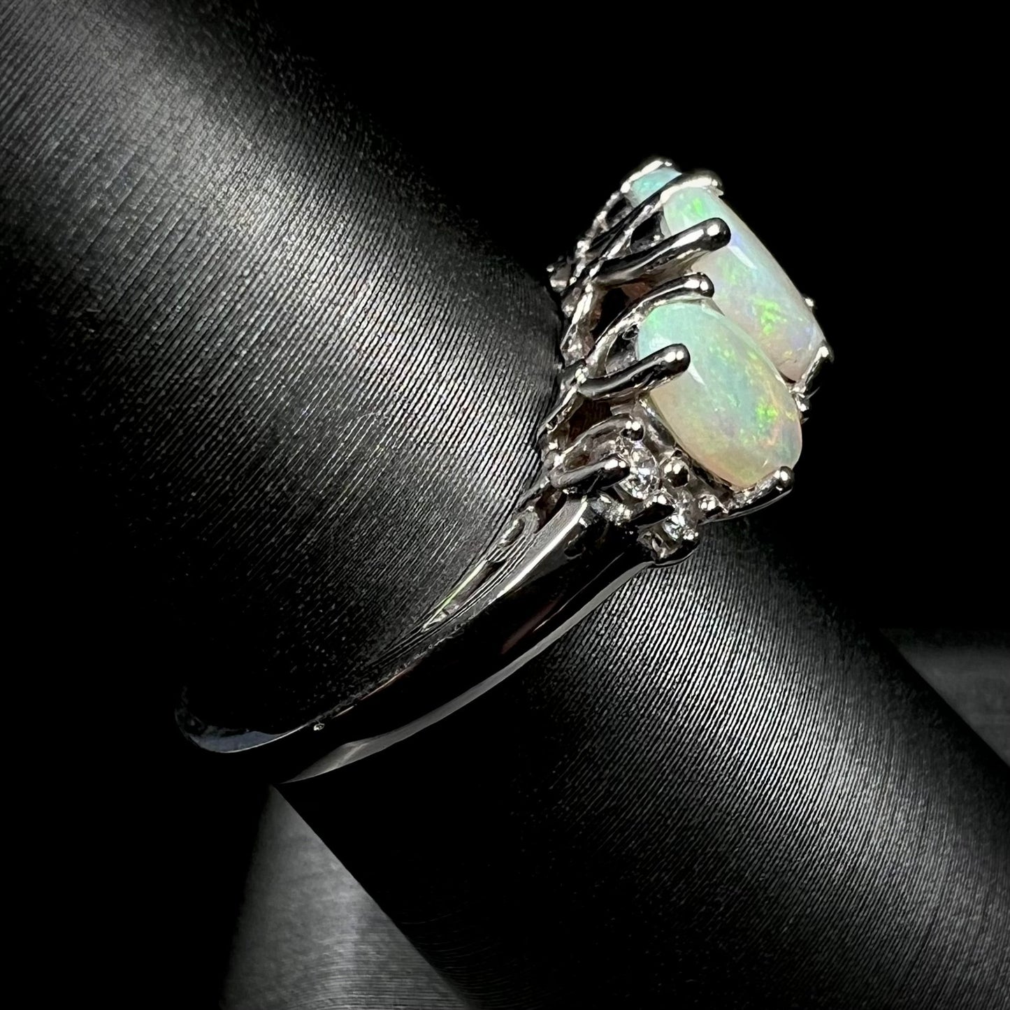 A ladies' white gold ring prong-set with three natural white opals and diamond accents. The opals play a green color.