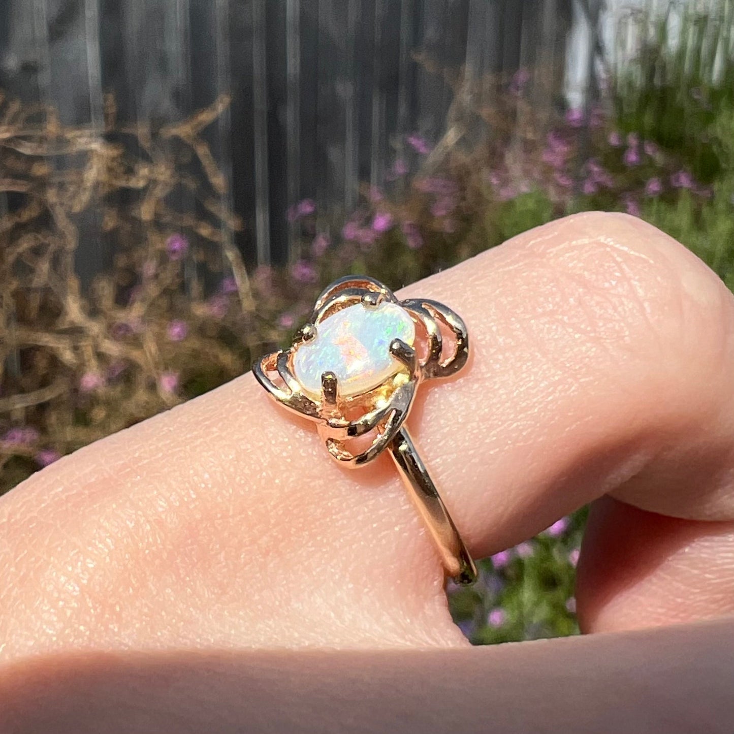 A yellow gold ring mounted with an oval cut opal. The opal has a white base tone with green and blue color play.