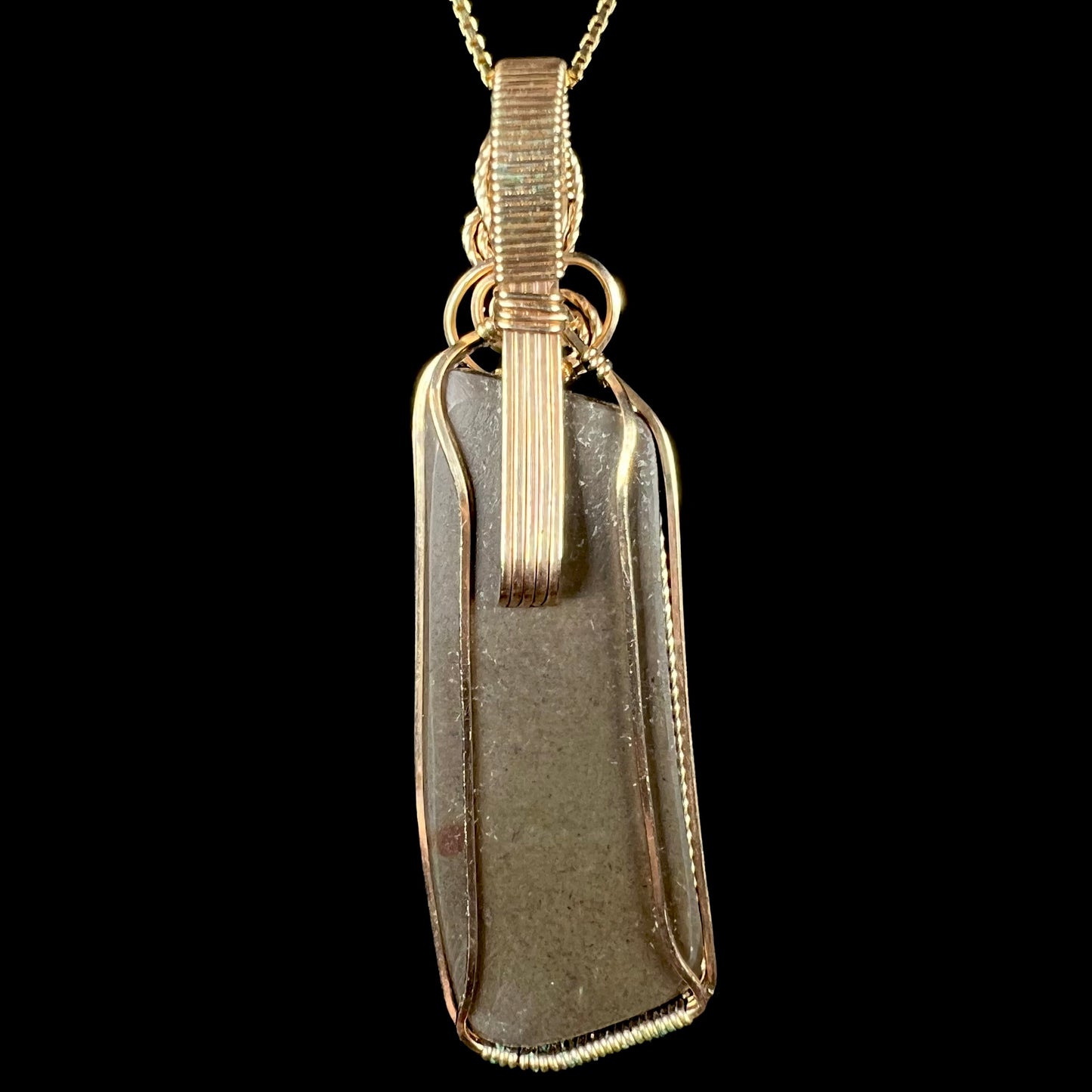 The back side of a wire wrapped ammolite pendant against a black background.