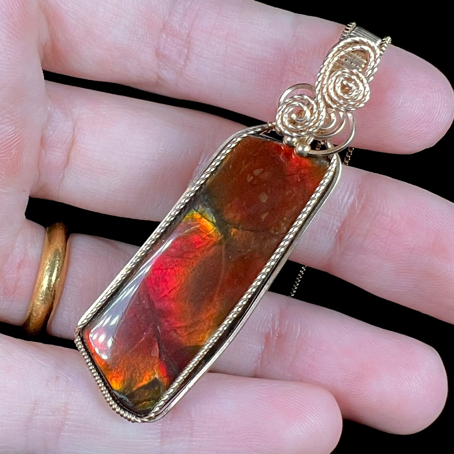 A wire wrapped red ammolite pendant held at an angle by a hand.
