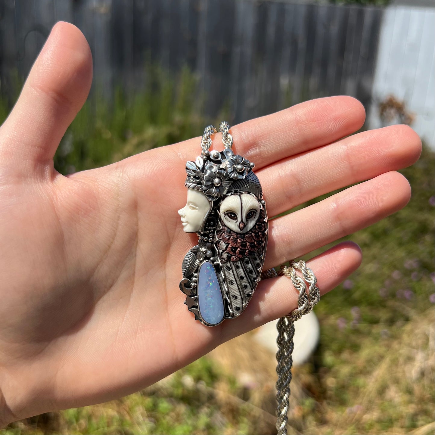 A woman and owl necklace with a nature-inspired motif shown in sunlight, made from sterling silver, bone, and an opal doublet.