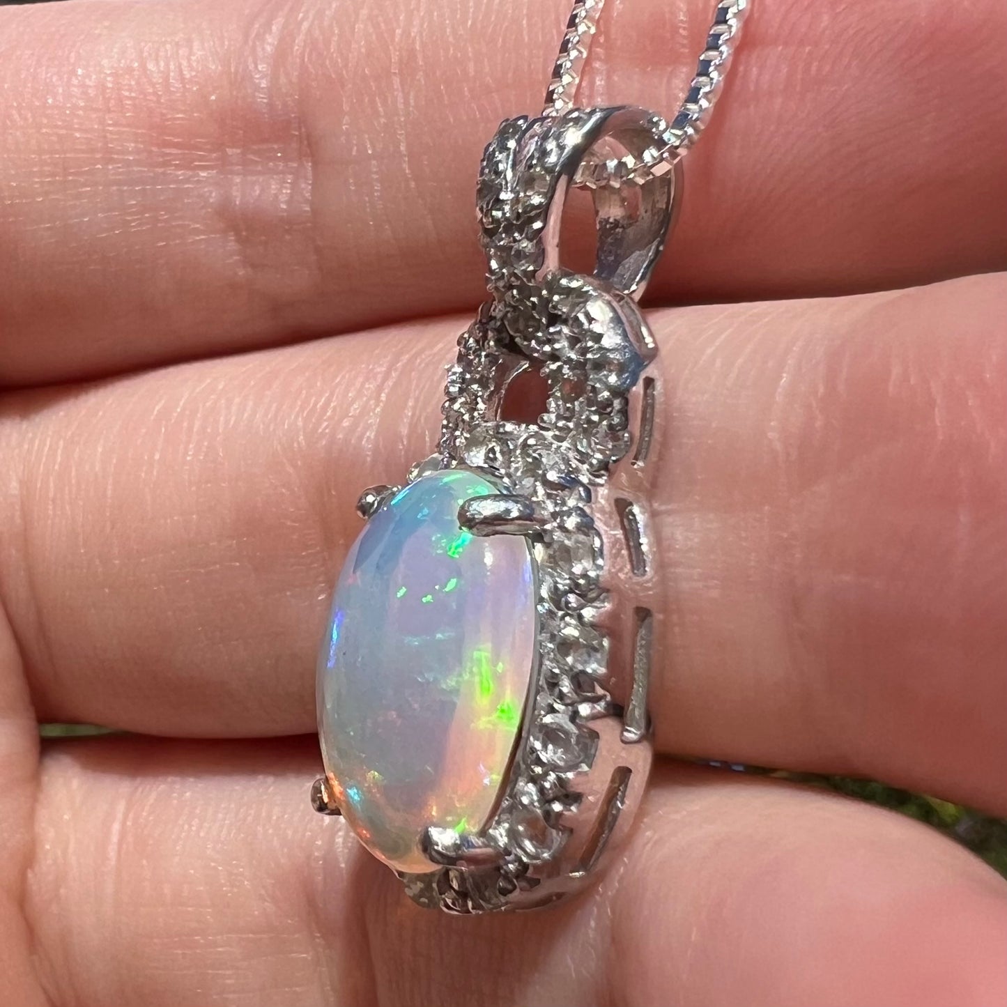 Side view of women's silver Ethiopian opal halo design pendant, held in hand under sunlight