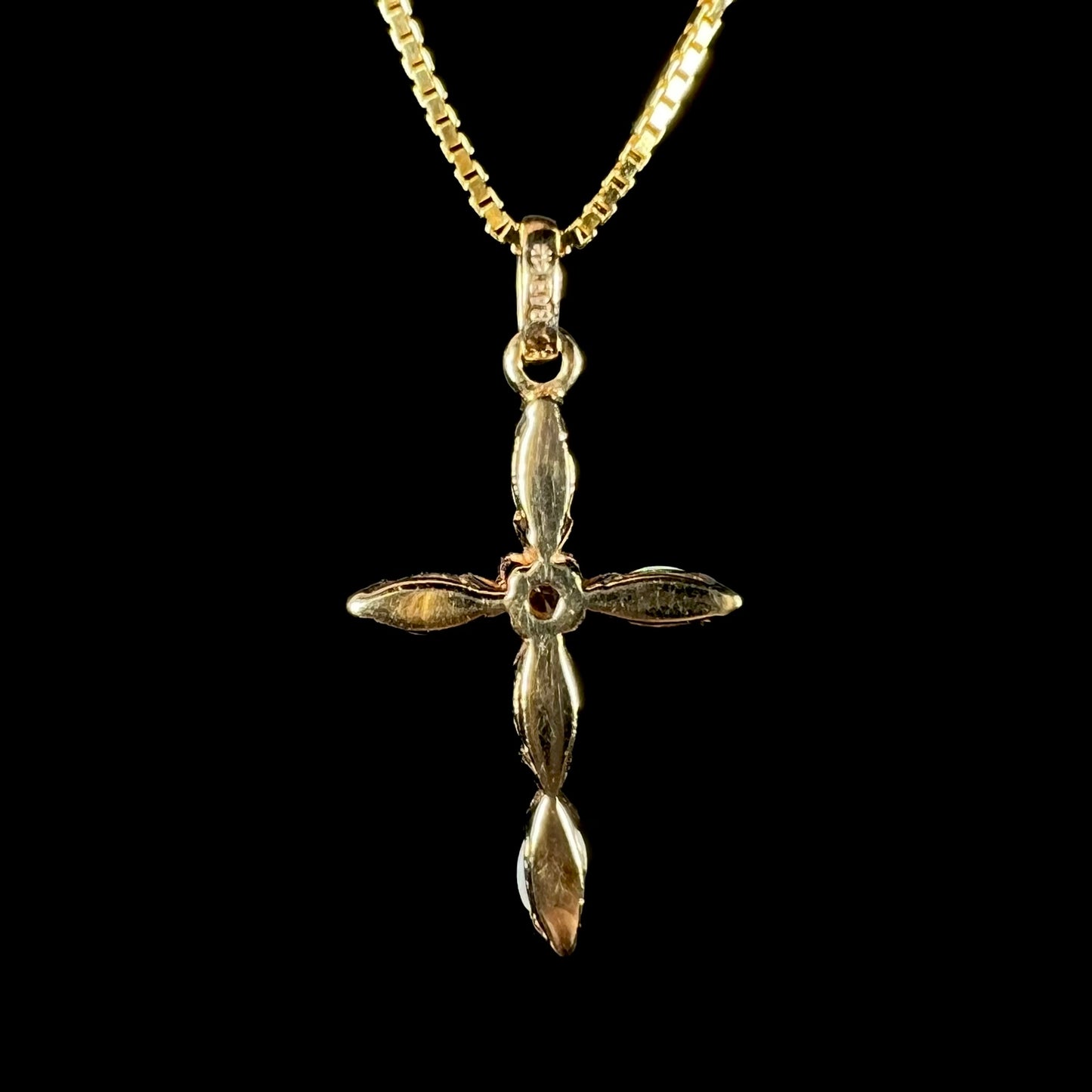 Back side of a yellow gold opal cross necklace against a black background. None of the opals are visible.