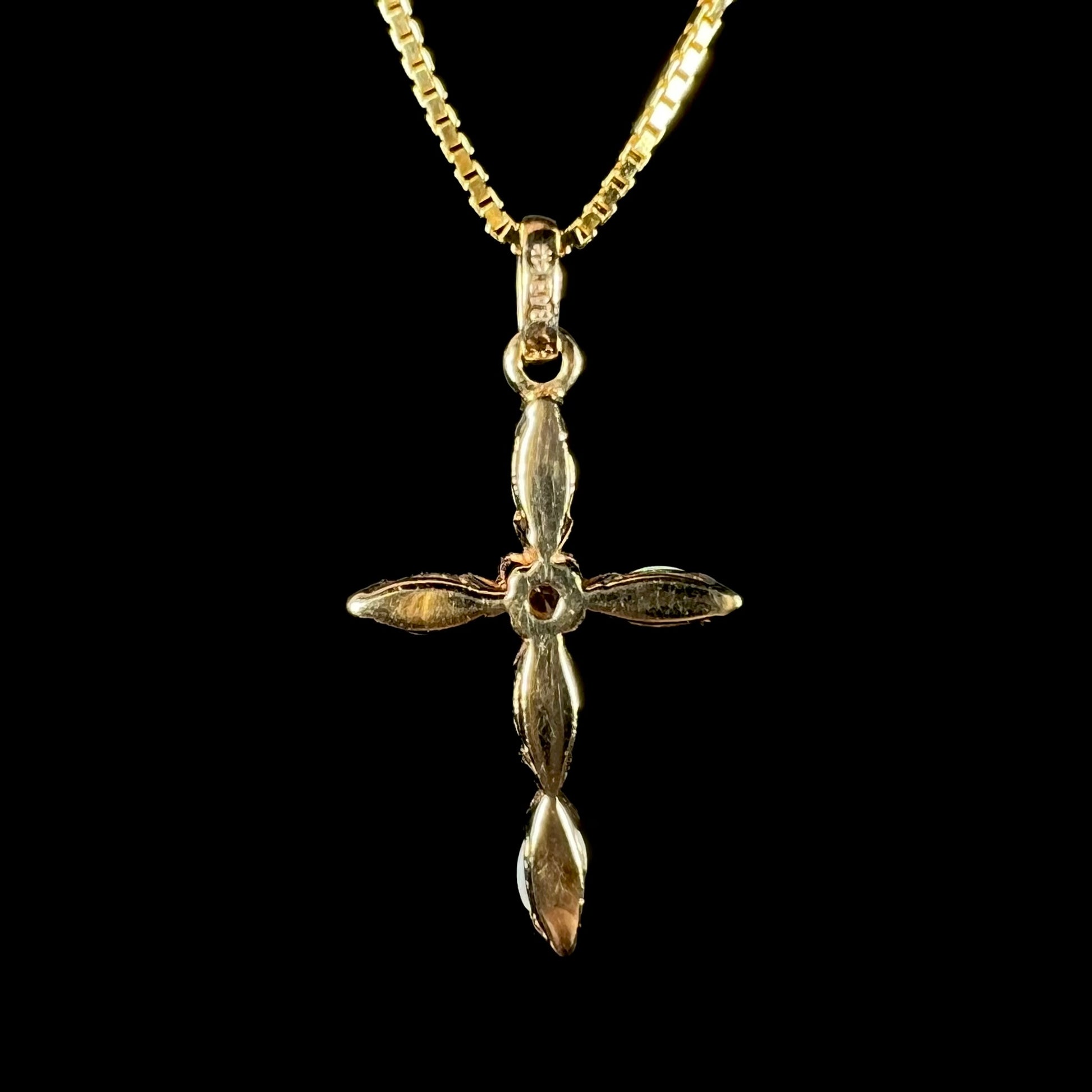 Back side of a yellow gold opal cross necklace against a black background.  None of the opals are visible.