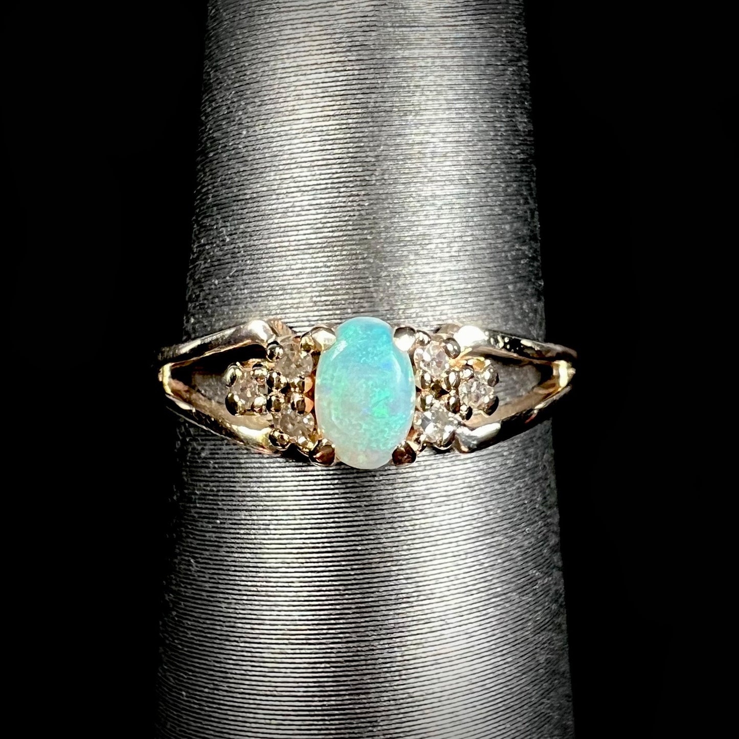 A ladies' yellow gold opal and diamond pinkie ring. The ring is a small size, and the opal shines green and blue colors.