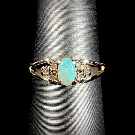 A ladies' yellow gold opal and diamond pinkie ring.  The ring is a small size, and the opal shines green and blue colors.