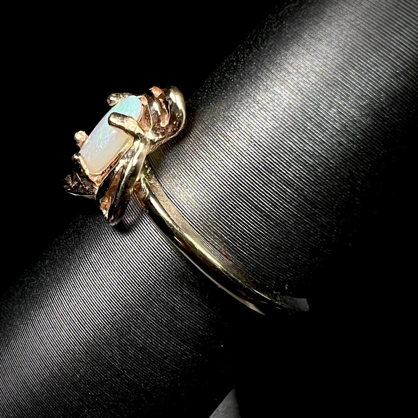 A yellow gold ring mounted with an oval cut opal. The opal has a white base tone with green and blue color play.