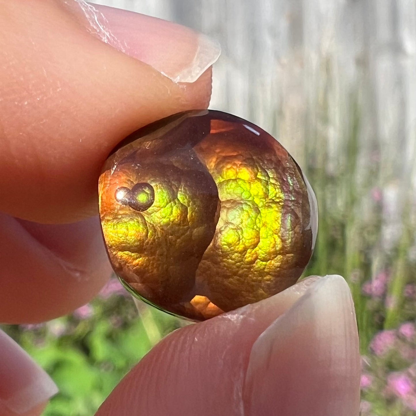 A loose, round Mexican fire agate stone. The stone shines colors of green, yellow, and orange.