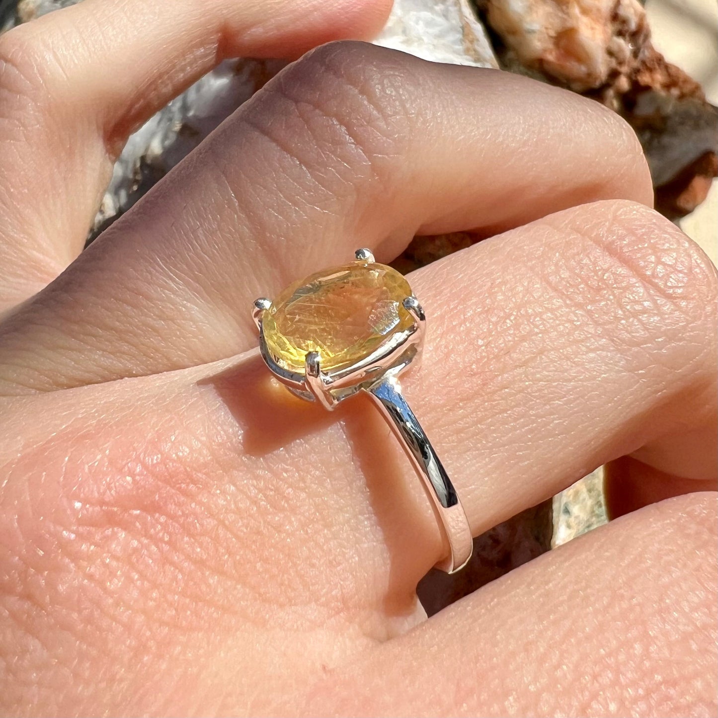 A silver solitaire ring prong-set with a natural, faceted oval cut Mexican fire opal. The stone is a light yellow color.