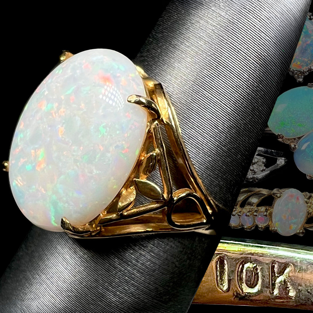 10k gold Australian opal cocktail ring shown on ring display from angle in front of faded opal rings and boldly visible "10K" hallmark stamp.