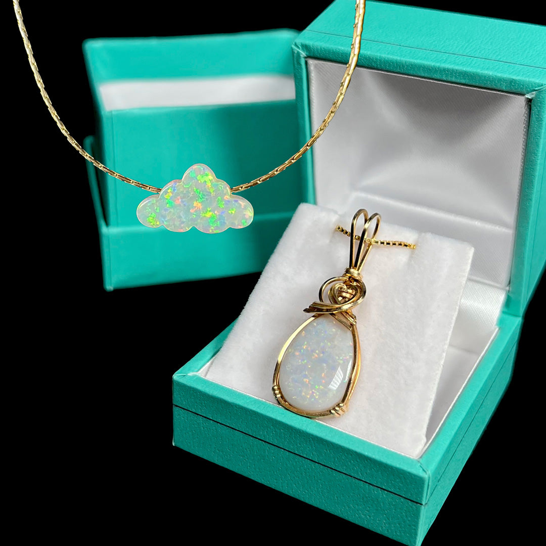 A gold-filled lab-created opal cloud carving necklace in front of a gold-filled Australian opal pendant in blue box.