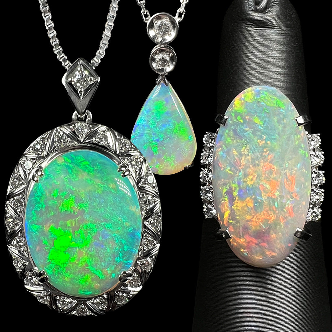 Two platinum Australian opal and diamond pendants—one larger oval shape and one smaller pear shape—shown hanging from chains against a black background next to a large Australian opal and diamond ring with orange fire on a ring display.
