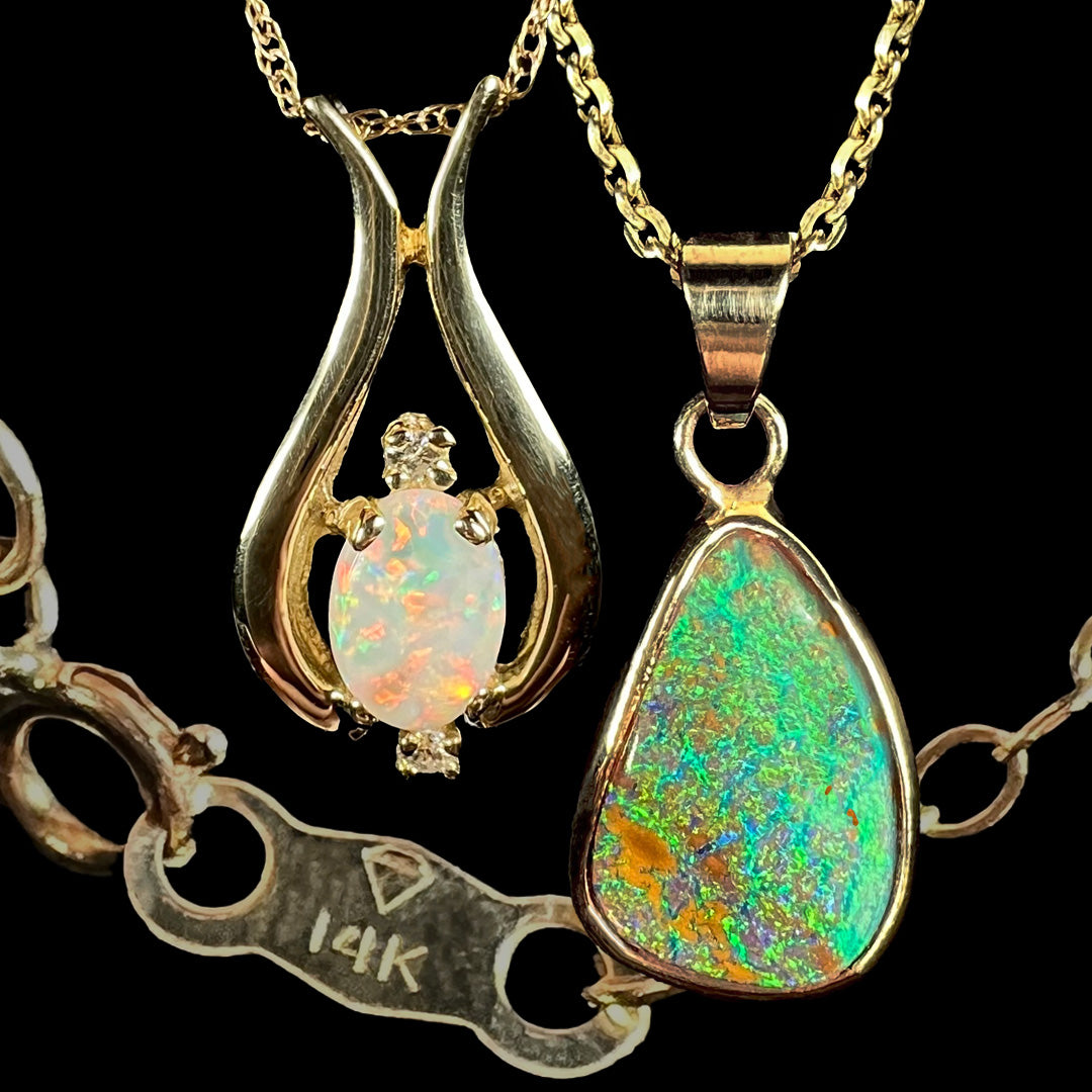 Two 14k yellow gold opal pendants shown close-up in front of faded gold chain tag stamped with "14K" hallmark.
